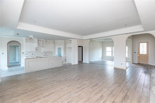 112 Shoalwater Way, Rockport, TX 78382 - unfurnished living room with a raised ceiling, arched walkways, light wood-style floors, and ornamental molding