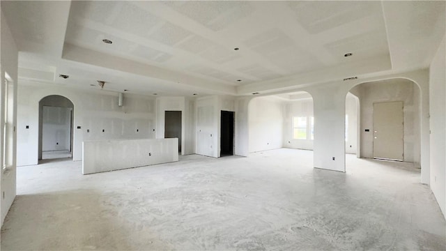 unfurnished room featuring a tray ceiling, concrete flooring, and arched walkways