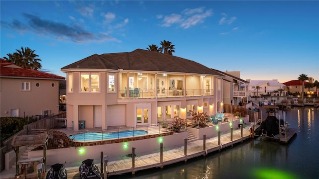 back house at dusk with a water view, a balcony, and a patio area