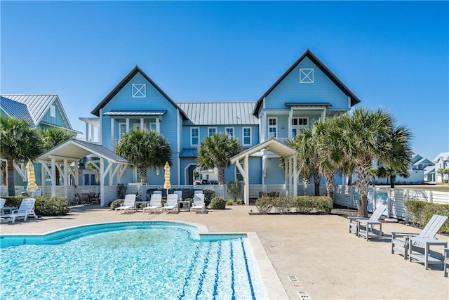 rear view of property with a standing seam roof, a patio area, metal roof, fence, and a community pool