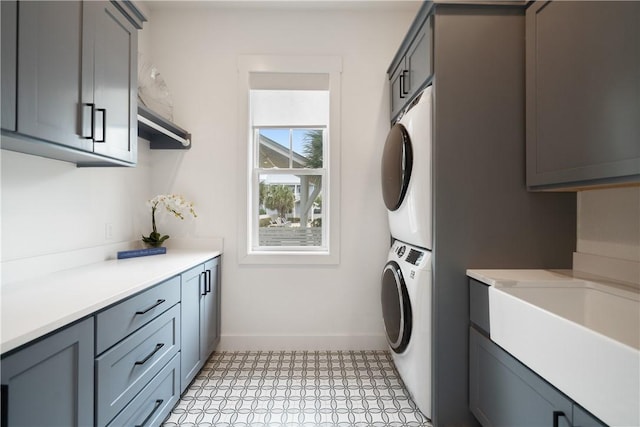 clothes washing area with baseboards, cabinet space, a sink, and stacked washing maching and dryer