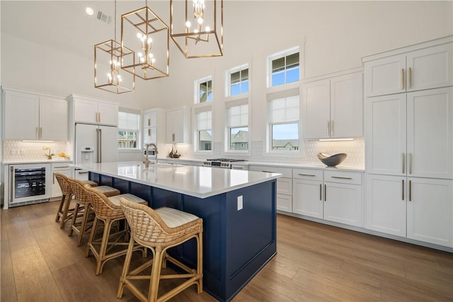 kitchen featuring visible vents, light wood-style flooring, wine cooler, high end white fridge, and a sink