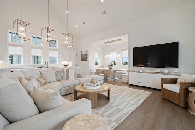 living room with high vaulted ceiling, a notable chandelier, visible vents, and wood finished floors