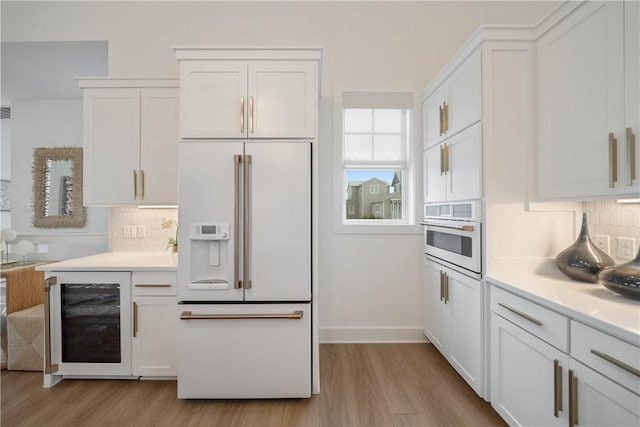 kitchen with white appliances, beverage cooler, white cabinets, decorative backsplash, and light wood-style flooring