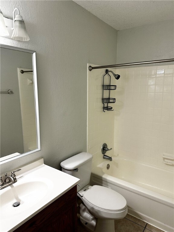 full bathroom featuring tile patterned floors, vanity, a textured ceiling, tiled shower / bath combo, and toilet