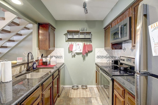 kitchen with tasteful backsplash, dark stone counters, appliances with stainless steel finishes, hardwood / wood-style floors, and sink