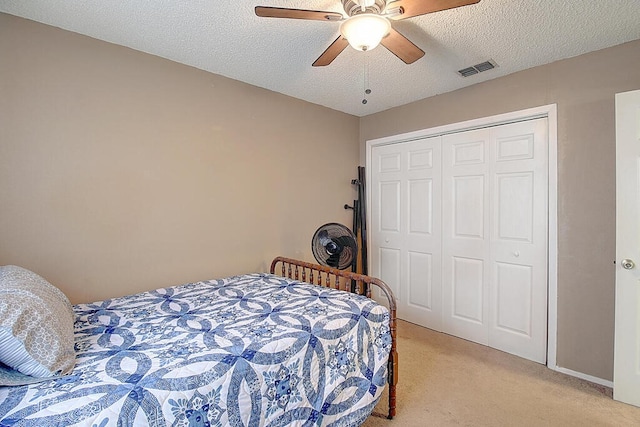 bedroom with a closet, a textured ceiling, light colored carpet, and ceiling fan