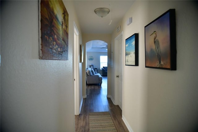 corridor featuring dark wood-style floors, baseboards, visible vents, and arched walkways