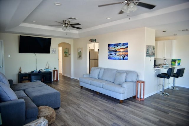 living room featuring arched walkways, dark wood-style flooring, a raised ceiling, and visible vents