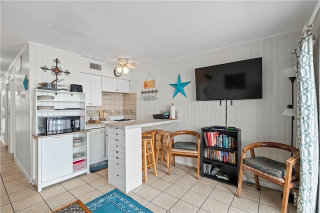 kitchen featuring tasteful backsplash, kitchen peninsula, white dishwasher, a breakfast bar, and white cabinets