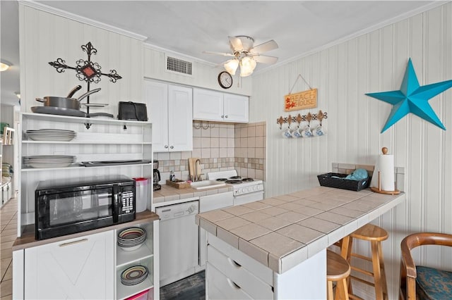 kitchen with white appliances, white cabinets, crown molding, decorative backsplash, and tile counters