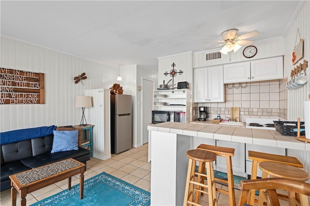 kitchen with tile counters, stainless steel fridge, a kitchen bar, decorative backsplash, and light tile patterned floors