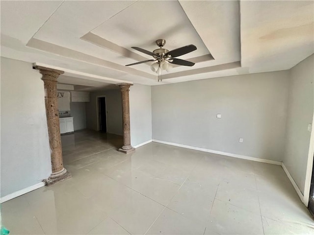 tiled empty room with ceiling fan, a raised ceiling, and decorative columns