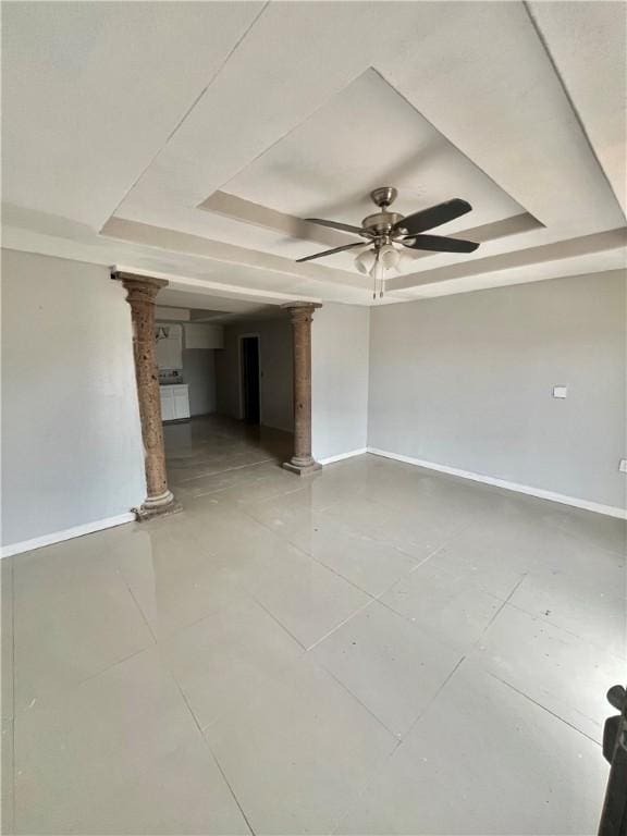 empty room with a tray ceiling, ceiling fan, and ornate columns