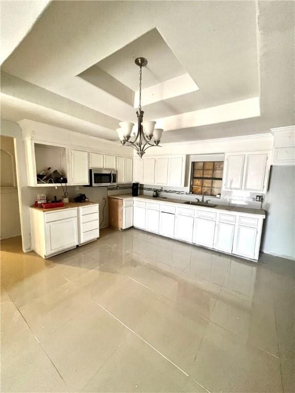 kitchen with pendant lighting, sink, white cabinetry, an inviting chandelier, and a tray ceiling