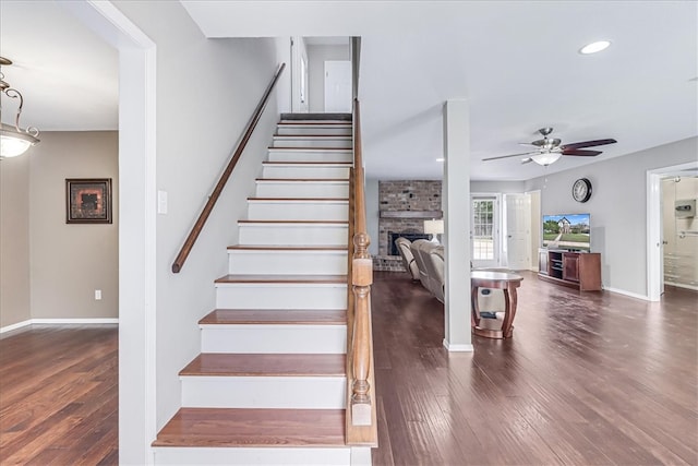 staircase featuring a fireplace, hardwood / wood-style flooring, and ceiling fan