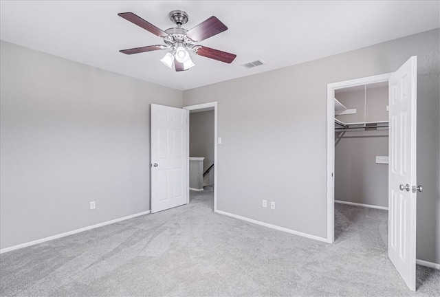 unfurnished bedroom with a closet, a spacious closet, ceiling fan, and light colored carpet