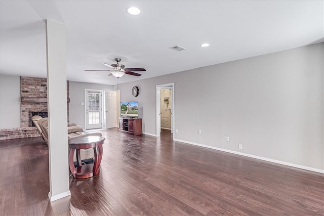 living room featuring ceiling fan, a fireplace, and dark wood-type flooring