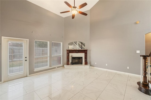 unfurnished living room with a fireplace, ceiling fan, and a high ceiling