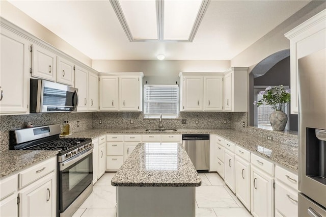 kitchen featuring sink, white cabinetry, stainless steel appliances, a center island, and light stone countertops