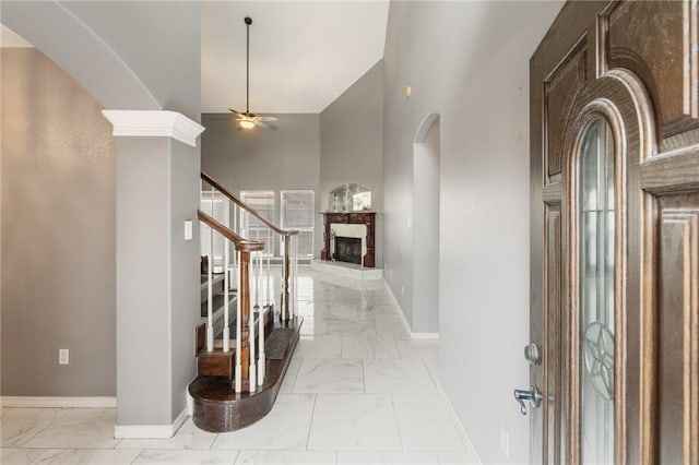 entrance foyer with ceiling fan, a stone fireplace, and a towering ceiling