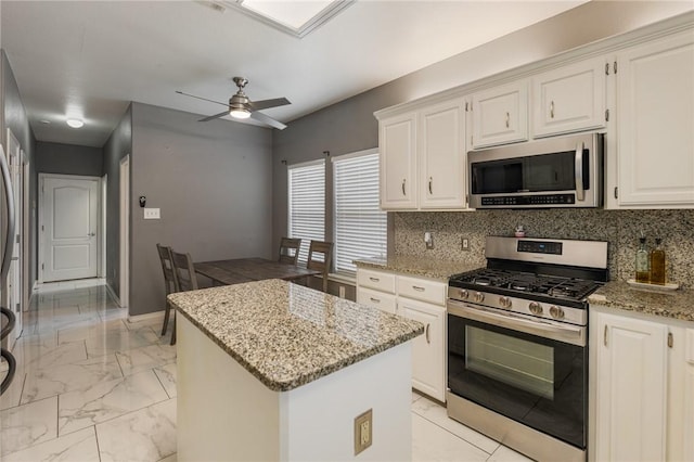 kitchen with tasteful backsplash, white cabinets, a center island, stainless steel appliances, and light stone countertops