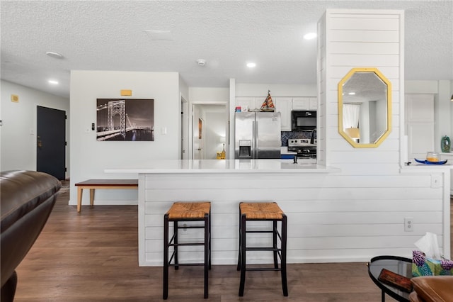 kitchen with dark wood-type flooring, white cabinets, a kitchen breakfast bar, kitchen peninsula, and stainless steel appliances