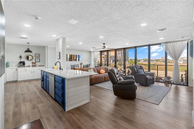 kitchen featuring a textured ceiling, light hardwood / wood-style floors, white cabinetry, and an island with sink