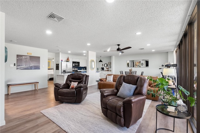 living room featuring ceiling fan, a textured ceiling, and light wood-type flooring