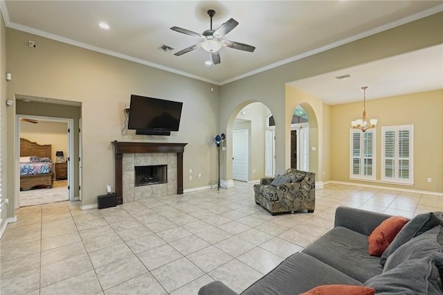 living area featuring visible vents, a tiled fireplace, ornamental molding, light tile patterned flooring, and ceiling fan with notable chandelier