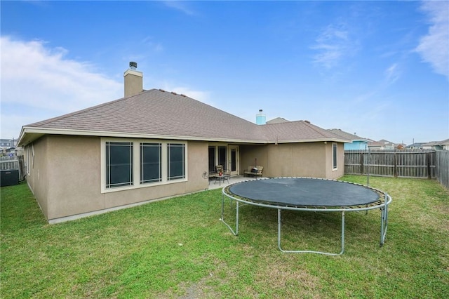 rear view of property featuring a trampoline, a fenced backyard, a lawn, and stucco siding