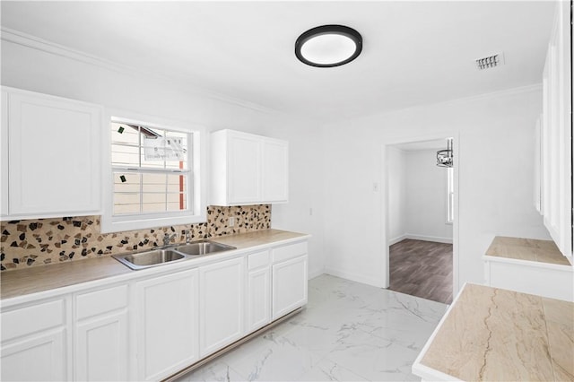 1113 Annapolis Dr, Corpus Christi, TX 78404 - kitchen featuring a sink, light marble finish flooring, ornamental molding, white cabinets, and backsplash