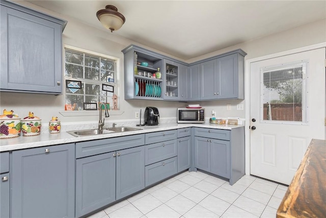 1124 Orange St, Mercedes, TX 78570 - kitchen featuring a sink, stainless steel microwave, glass insert cabinets, light countertops, and light tile patterned floors