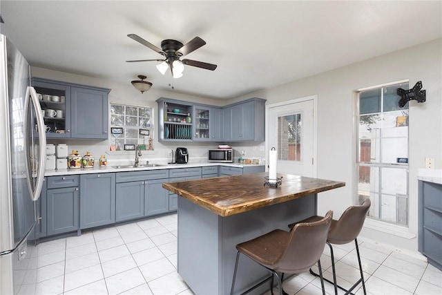 1124 Orange St, Mercedes, TX 78570 - kitchen with stainless steel appliances, a sink, light tile patterned flooring, a kitchen breakfast bar, and glass insert cabinets