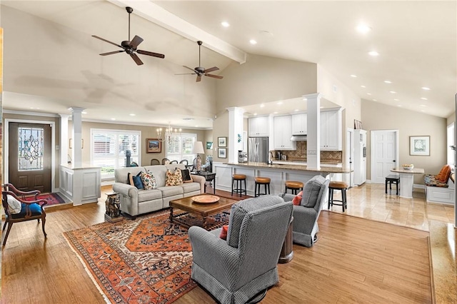 living area featuring light wood-style floors, high vaulted ceiling, beamed ceiling, ornate columns, and ceiling fan with notable chandelier