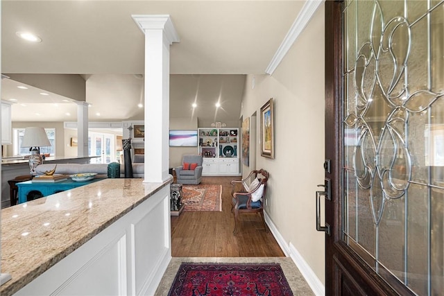 kitchen with decorative columns, white cabinets, light stone counters, wood finished floors, and crown molding