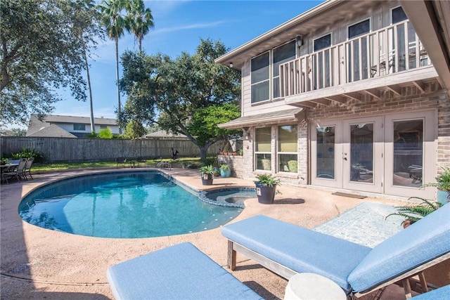 view of swimming pool featuring a pool with connected hot tub, fence, french doors, and a patio