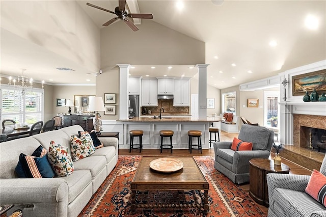 living area with wood finished floors, a fireplace, decorative columns, and ceiling fan with notable chandelier