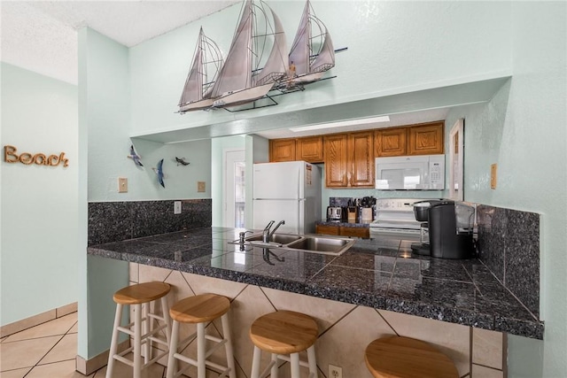 kitchen featuring white appliances, tile counters, brown cabinetry, a peninsula, and a sink