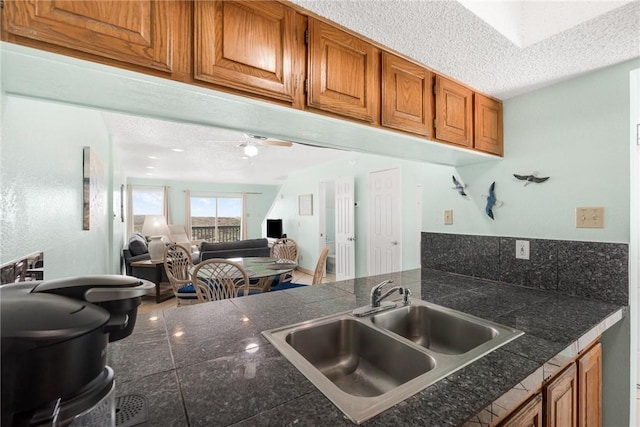 kitchen featuring a textured ceiling, tile counters, brown cabinetry, and a sink