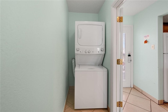 clothes washing area with light tile patterned floors, stacked washer and dryer, a textured ceiling, laundry area, and baseboards