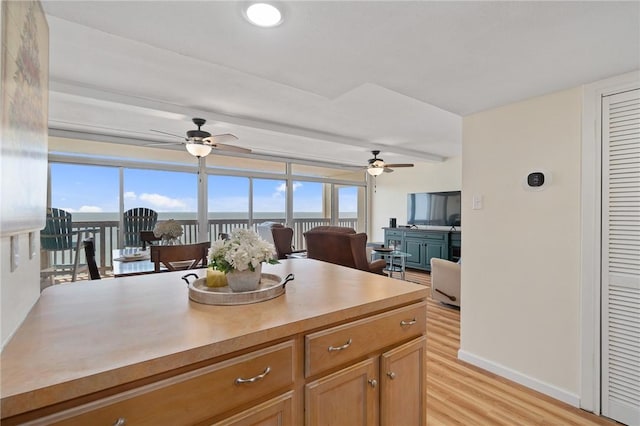 kitchen featuring baseboards, ceiling fan, open floor plan, light countertops, and light wood-style flooring