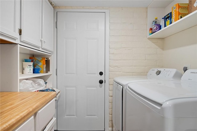 washroom featuring cabinet space, washing machine and dryer, and brick wall