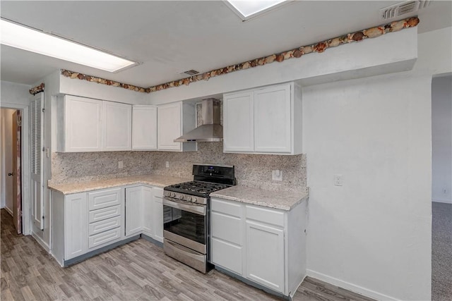 2406 Lakeview Dr, Rockport, TX 78382 - kitchen featuring wall chimney range hood, stainless steel gas range, light wood-style flooring, decorative backsplash, and white cabinets