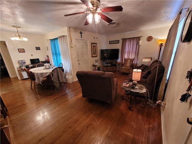 living room with dark wood-type flooring, ceiling fan with notable chandelier, and a textured ceiling