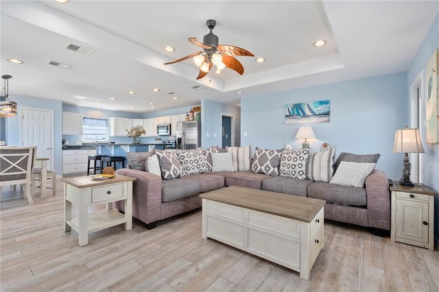 living room with light wood-type flooring, a raised ceiling, visible vents, and recessed lighting