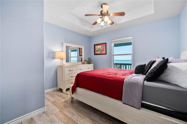 bedroom featuring light wood finished floors, ceiling fan, a tray ceiling, and baseboards