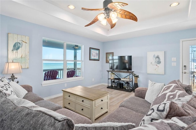 living room featuring ceiling fan, recessed lighting, baseboards, light wood-style floors, and a tray ceiling