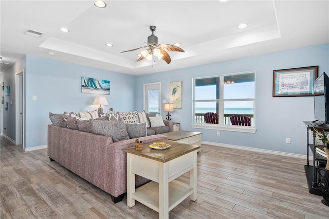 living room featuring a tray ceiling, visible vents, light wood-style flooring, and baseboards