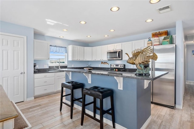 kitchen with a breakfast bar, visible vents, light wood-style floors, white cabinetry, and appliances with stainless steel finishes